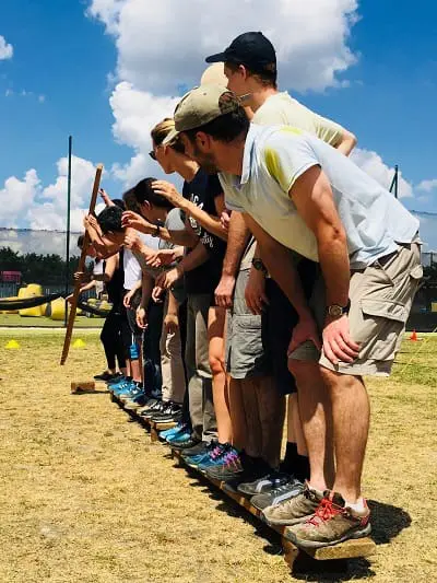 Groupe de participants avançant ensemble sur une planche lors d’un défi de coopération en plein air