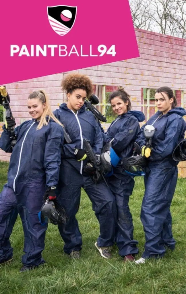 Quatre participantes en combinaison bleue posant avec leur équipement de paintball devant un parcours extérieur Paintball94