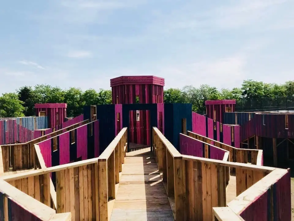 Parcours de paintball en bois peint en rose et bleu, composé de passerelles, couloirs et tours en plein air