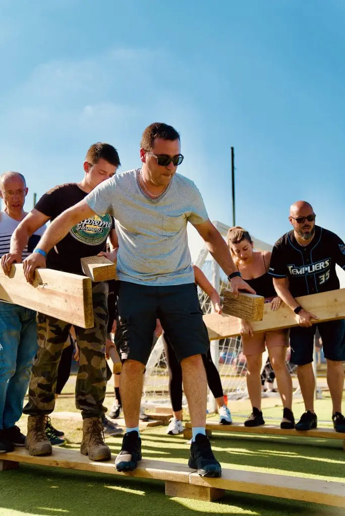 Participants avançant en équipe sur des planches en bois lors d’une activité de cohésion en plein air.
